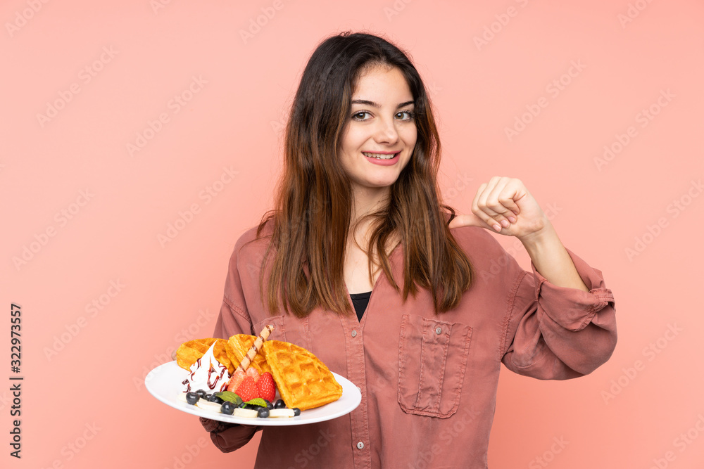 Young caucasian woman holding waffles isolated on pink background proud and self-satisfied