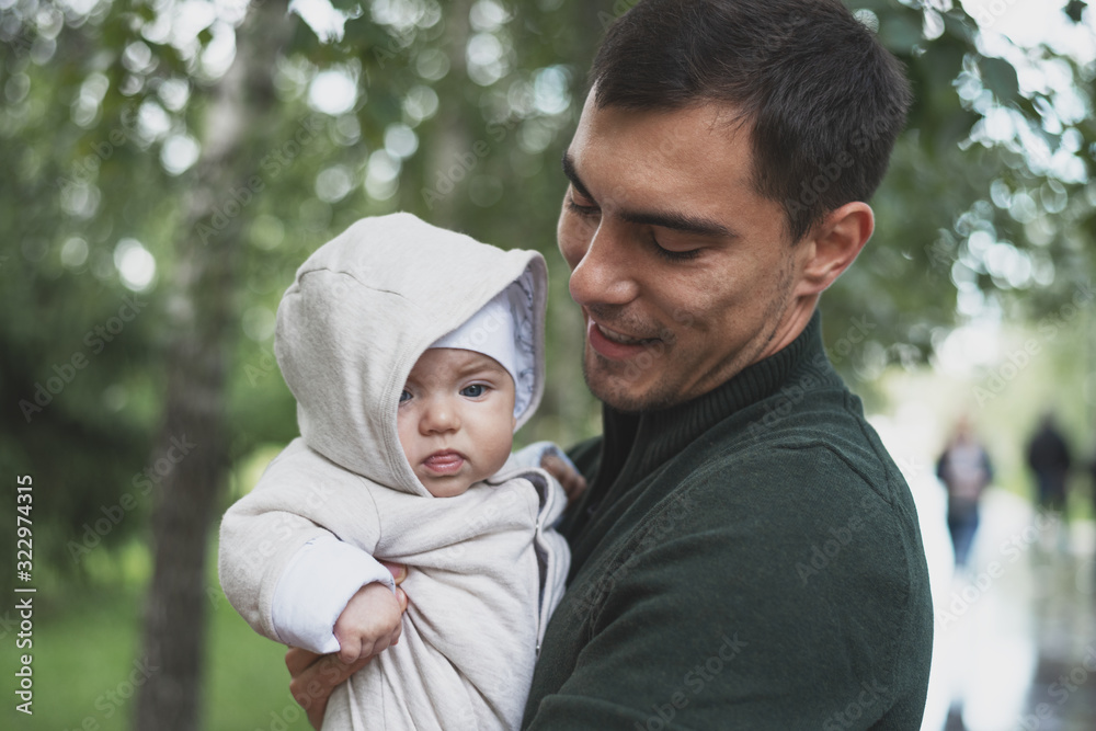 brunette dad in green jacket with baby in his arms in Park brunette dad in green jacket with baby in his arms in Park