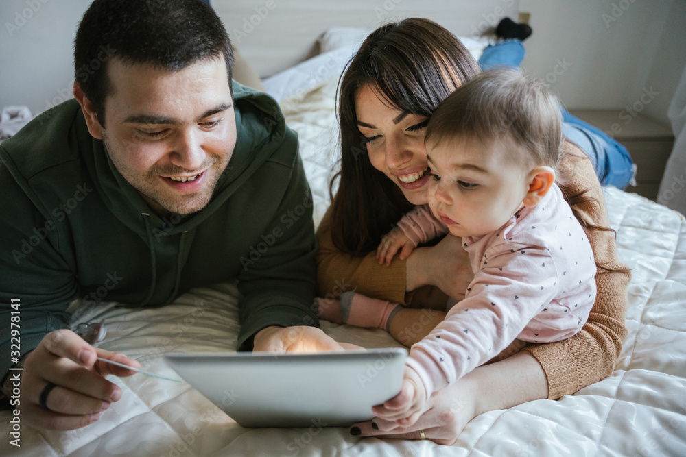 Portrait of a family on the bed looking at the tablet with their baby girl and shopping online with a credit card - Father, mother and little daughter have fun together - Intimacy moment Portrait of a family on the bed looking at the tablet with their baby girl and shopping online with a credit card - Father, mother and little daughter have fun together - Intimacy moment