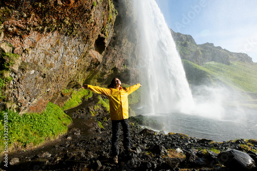Happy tourist under Seljalandfoss waterfall, Iceland (water splashes all around)