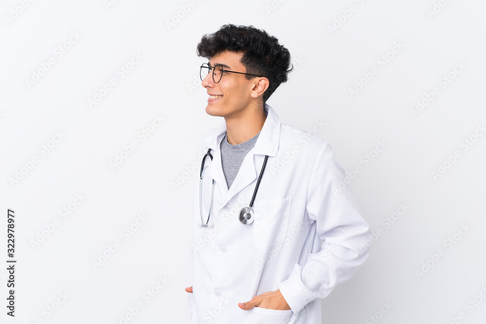 Young Argentinian man over isolated white background wearing a doctor gown and with stethoscope