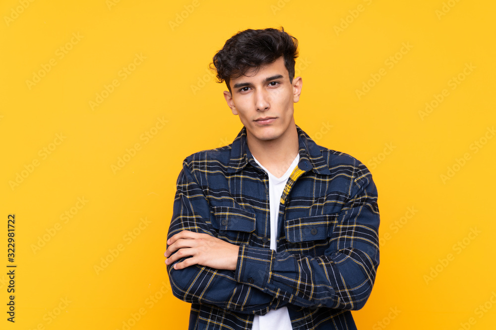 Young Argentinian man over isolated yellow background keeping arms crossed Young Argentinian man over isolated yellow background keeping arms crossed