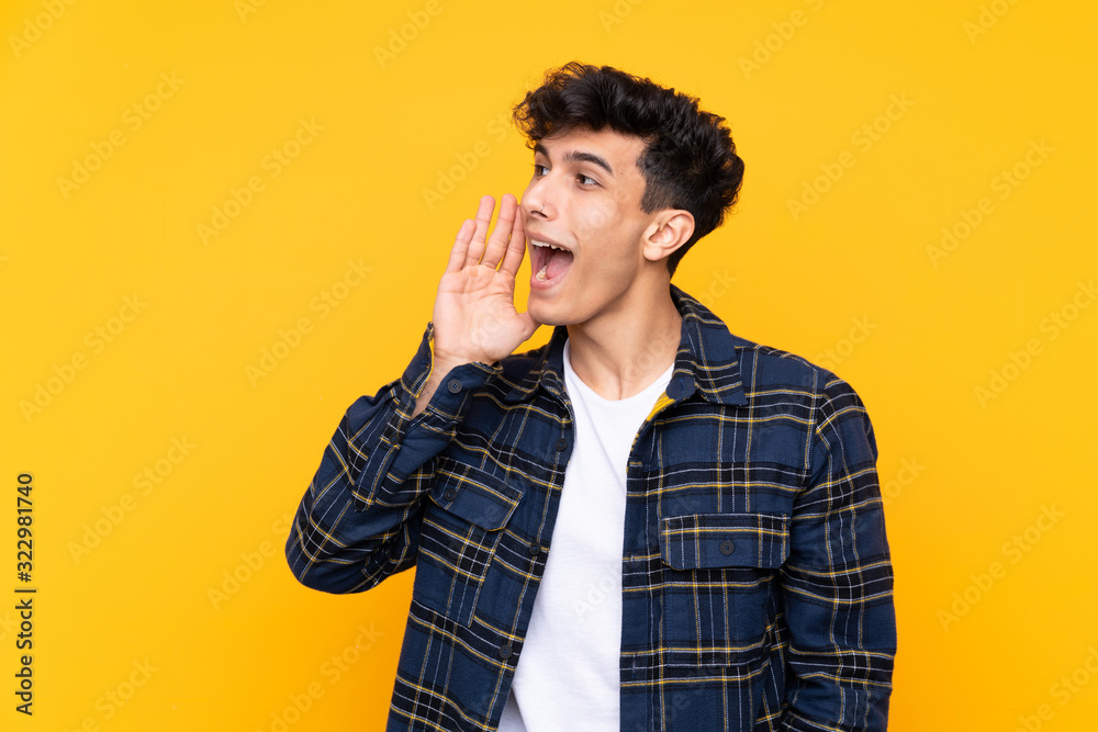 Young Argentinian man over isolated yellow background shouting with mouth wide open Young Argentinian man over isolated yellow background shouting with mouth wide open