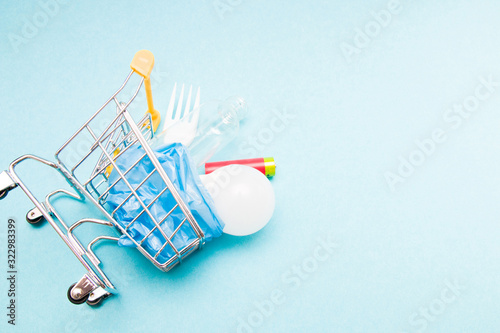 disposable plastic white plug, battery, light bulb and bottle in a shopping trolley on a blue background copy space, zero waste life style concept, garbage for recycling, eco consciousness