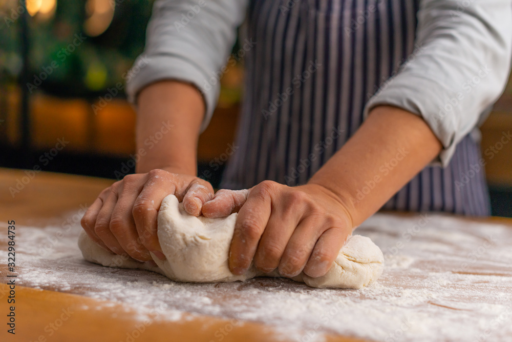 Close up of two female chef hands kneading pizza dough in a rustic style kitchen.