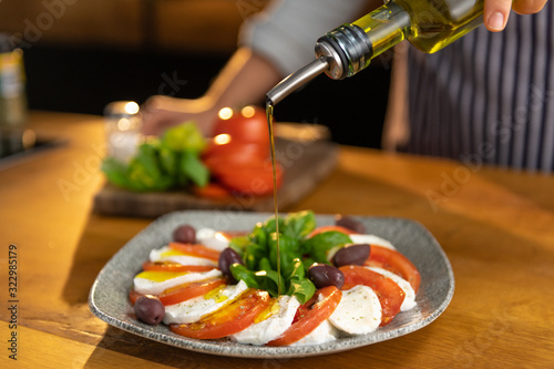 Closeup of female chef pouring olive oil over a freshly made, tasty mozzarella and tomato salad. photo