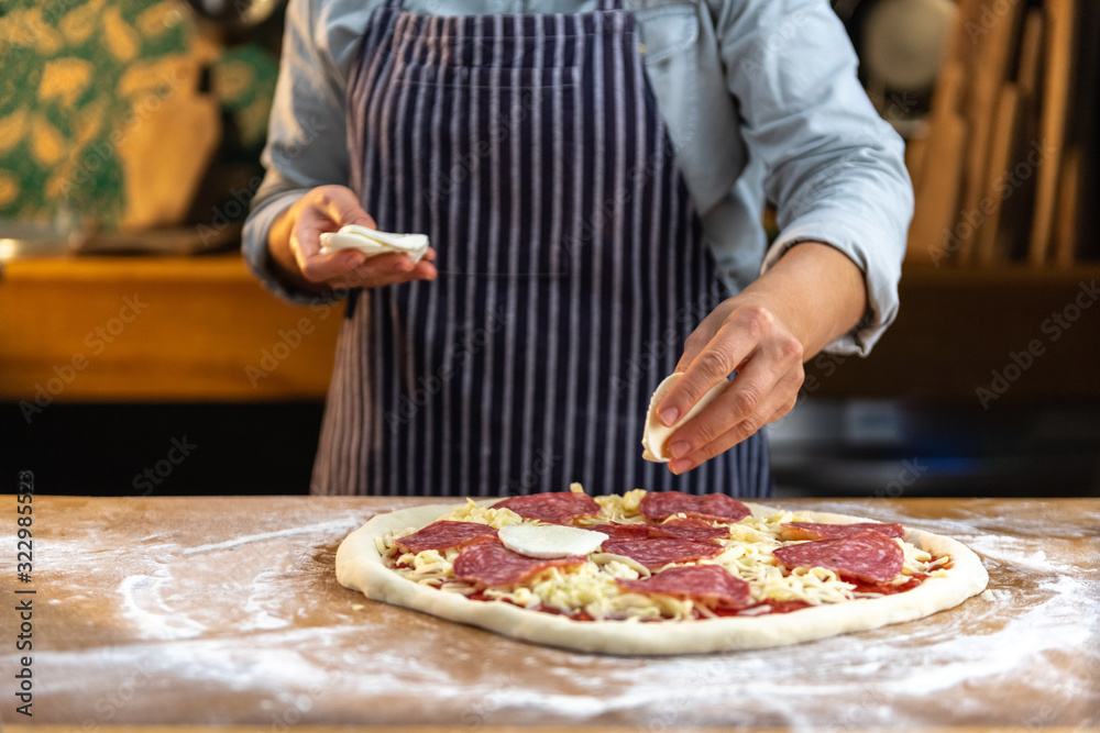 Female chef is placing slices of fresh mozzarella cheese on traditional, homemade pizza.