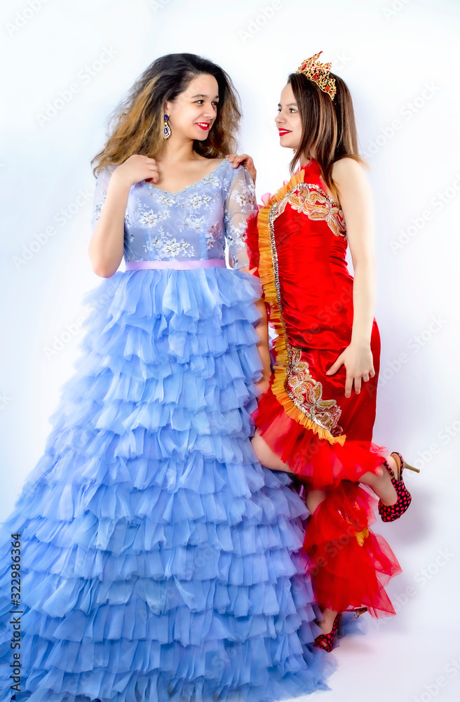 Two happy young woman in colorful clothes smiling and looking at each other, isolated over pink background. Isolate