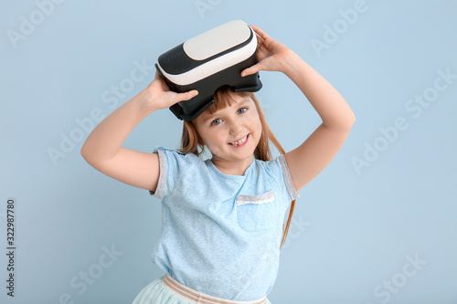 Little girl with virtual reality glasses on color background