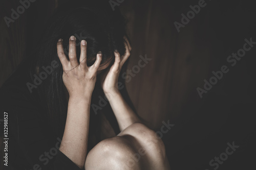 A woman hiding face. Violence against women concept. Depressed teenager sitting holding head in hands, stressed sad young woman having mental problems.