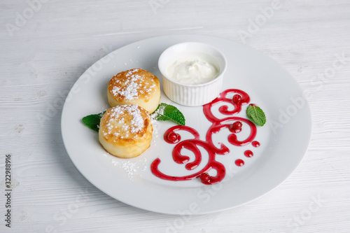 Cottage cheese pancakes or cheesecakes with sour cream on a white ceramic plate are decorated with jam. Delicious Breakfast or brunch. Menu