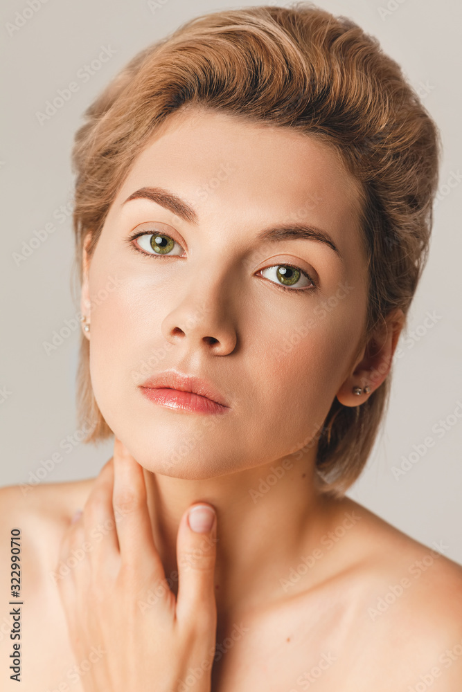 Attractive blonde model with a short haircut and green eyes looks at the camera. Close-up, retouch, shot in the studio on a light background. Skin Care Concept 25+