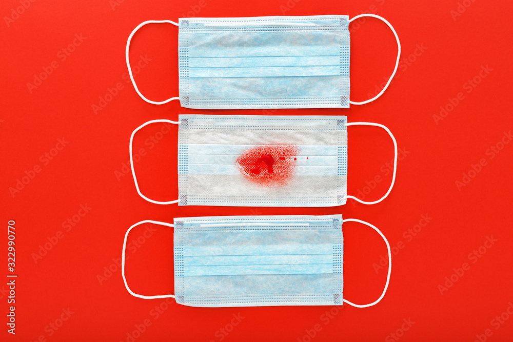 Hemoptysis, coronavirus, protective surgical masks with blood on red background. Pneumonia