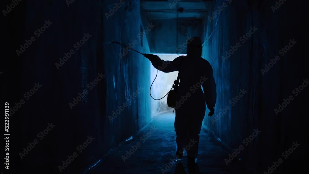 Worker wearing protective suit sprays disinfectant liquid in medical lab