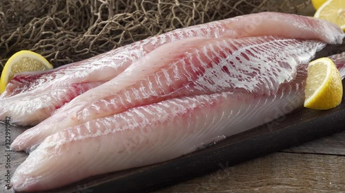 Fresh haddock fillets on a cutting board with lemon wedges. photo