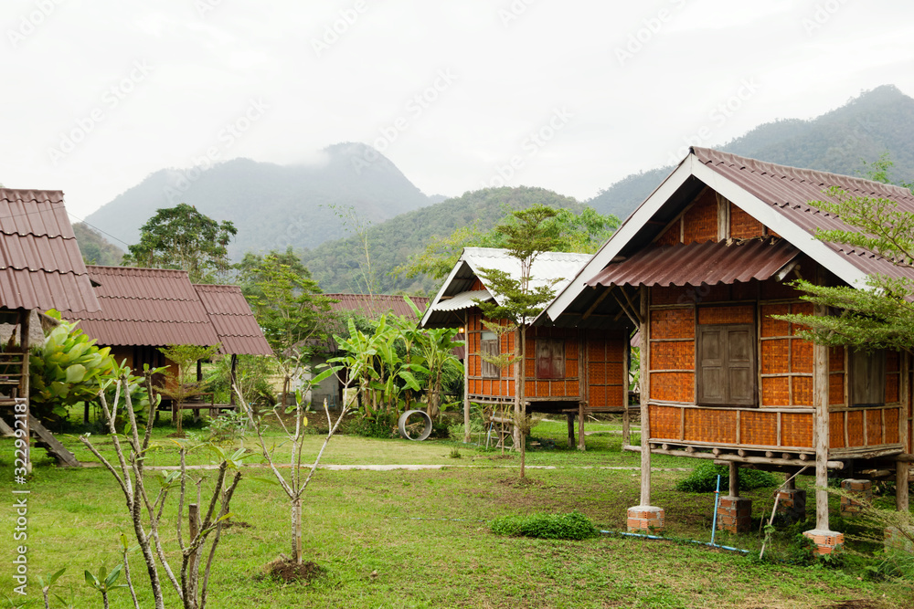 View on wooden houses and garden on a background of mountains in cloudy weather. Pai, Mae Hong Soon Province, Thailand.