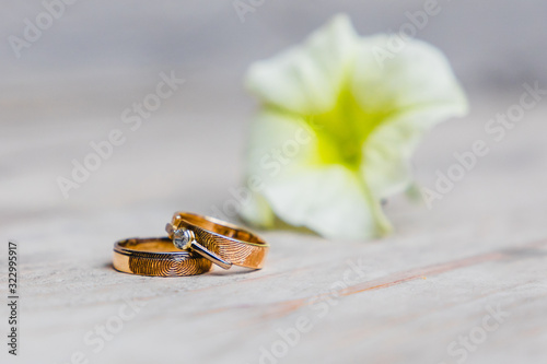 Golden weddingrings on a wooden plate with fingerprint engraving and a flower in the background photo