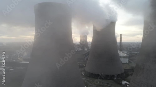 Aerial close dolly left reveal UK power station cooling towers under smoke steam emissions with sunrise lens flare..
