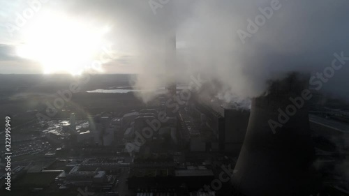 Aerial descending away from UK power station cooling towers smoke steam emissions at sunrise.