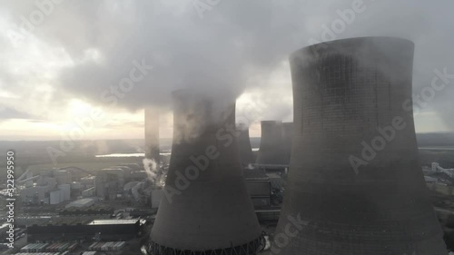 Aerial dolly right view across global power station cooling towers smoke steam emissions at sunrise.