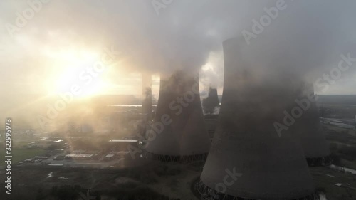 Aerial slow dolly left view of UK power station cooling towers smoke steam emissions at sunrise.