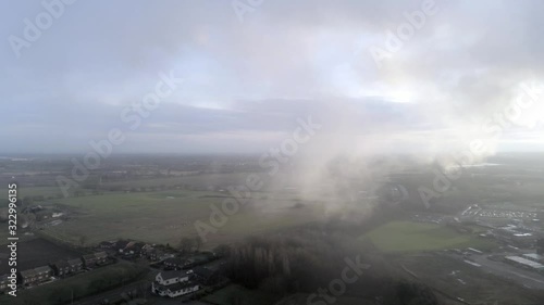 Aerial view of UK countryside panning right to power station cooling towers smoke steam emissions at sunrise.