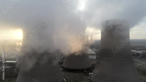 Aerial slow dolly left view across power station cooling towers under smoke steam emissions at sunrise.