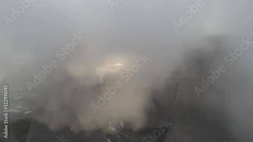 Aerial shot tilt down to UK power station cooling towers smoke steam emissions at sunrise.