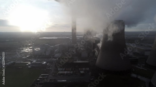 Aerial lowering pull back UK power station cooling towers below smoke steam emissions at sunrise.