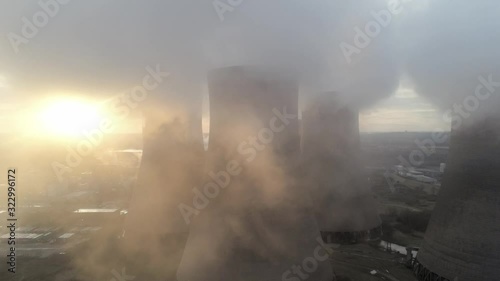 Aerial view of UK power station cooling towers dolly left across smoke steam emissions at sunrise.