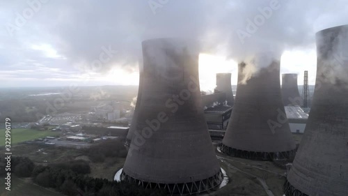Aerial wide dolly left across UK power station cooling towers under smoke steam emissions at sunrise.