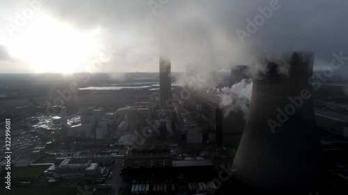 Aerial view of UK power station cooling towers flying through smoke steam emissions at sunrise.