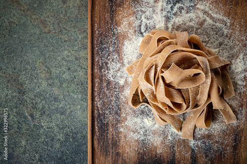 Uncooked brown pasta tagliatelle with chestnuts on a wooden Board with flour, top view and copy space