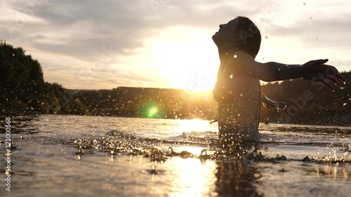 playful girl splashes her long hair in a refreshing summer evening near tropical island with refreshing river water. girl flips back hair. beautiful spray of water in rays of sunset. splash of water