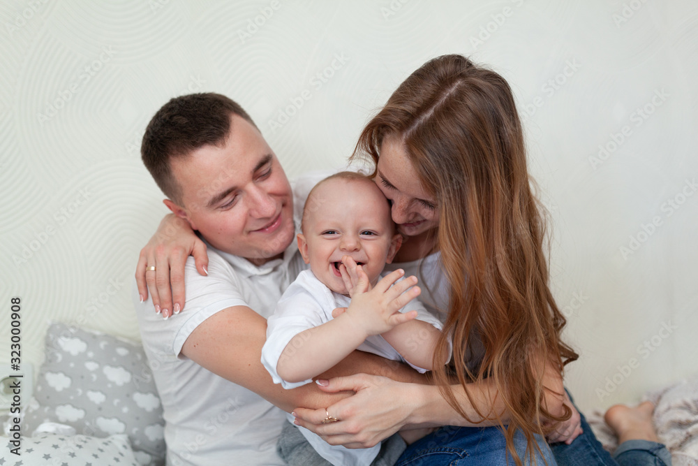 Portrait of a happy young family. Parents and baby hugging and playing on the sofa in the room Portrait of a happy young family. Parents and baby hugging and playing on the sofa in the room