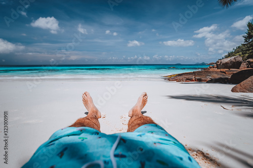 POV of male wearing swimming shorts with tanned legs on paradise white sand tropical exotic beach with view to turquoise blue ocean. Travel holidays vacation concept photo