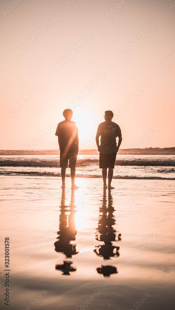 pareja de hombres parados en la orilla de la playa mirando al atardecer  Stock Photo | Adobe Stock