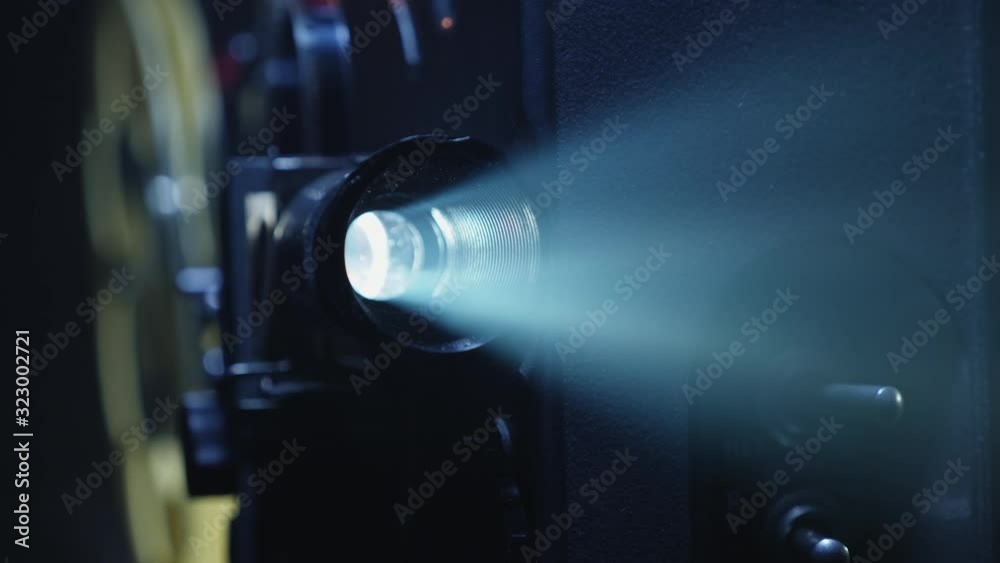 Close-up of a projector lens with a ray of light. Working 8mm retro film projector in a dark room