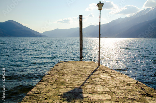 Pier on an Alpine Lake Maggiore with Mountain and Street Lamp with Shadow in Ascona, Switzerland. photo