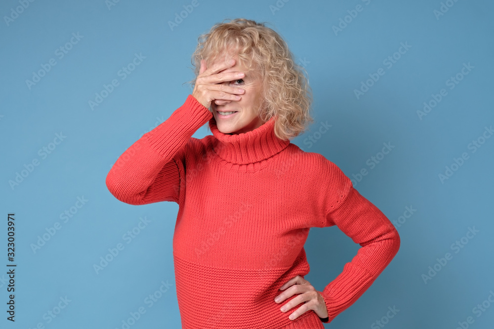 Shy timid senior woman covering face with hands and peeping through her fingers at camera being curious. Studio shot Shy timid senior woman covering face with hands and peeping through her fingers at camera being curious. Studio shot