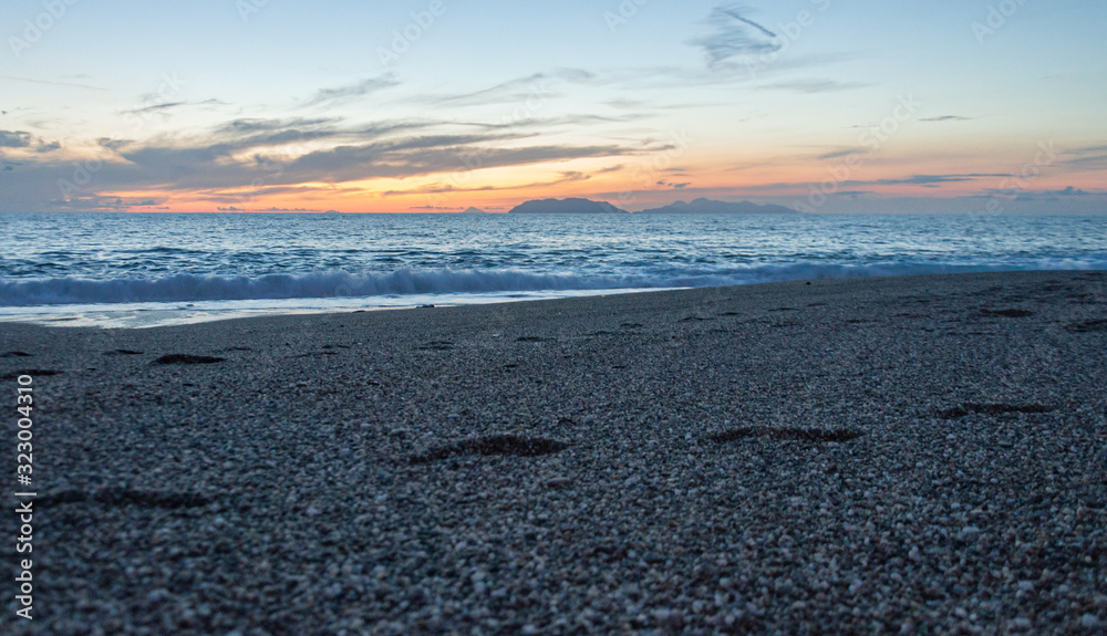 Footprints in the sand of Milazzo beach during the sunset. Aeolian islands are in the background. Selective focus on the wave. Grainy style. Sicily, Italy