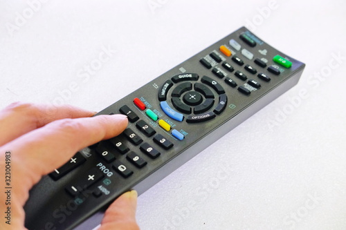 a person's hand presses the control buttons of the TV black remote at their leisure with their finger to change the lcd video channel