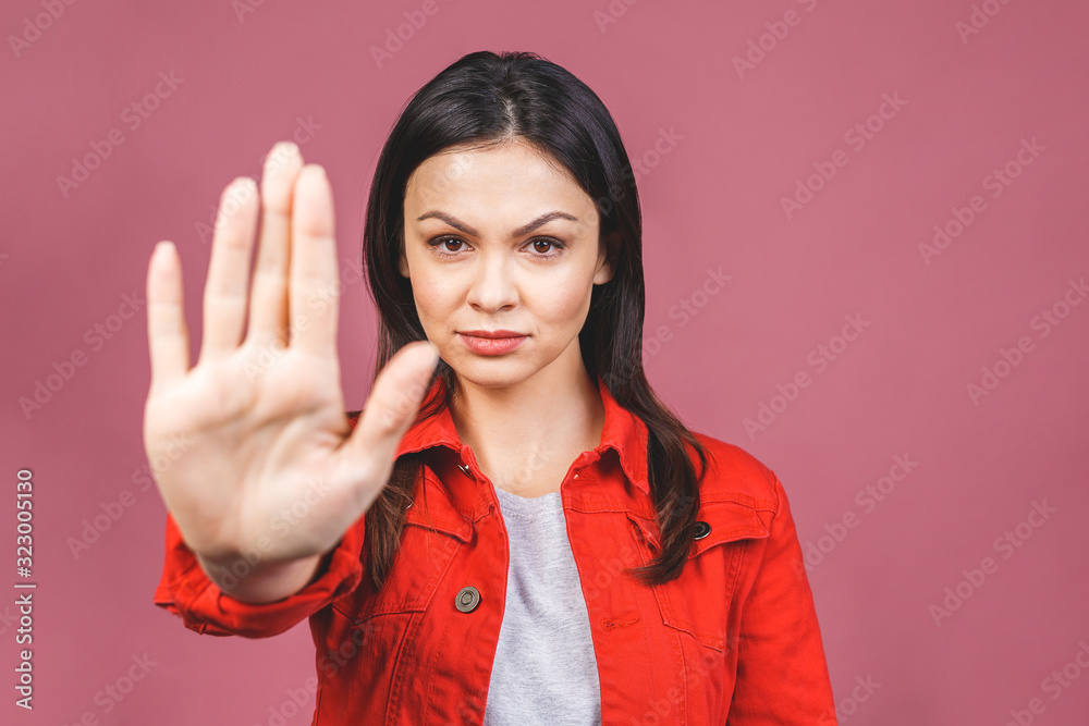 Portrait of a serious young woman standing with outstretched hand showing stop gesture sign isolated over pink background. Portrait of a serious young woman standing with outstretched hand showing stop gesture sign isolated over pink background.