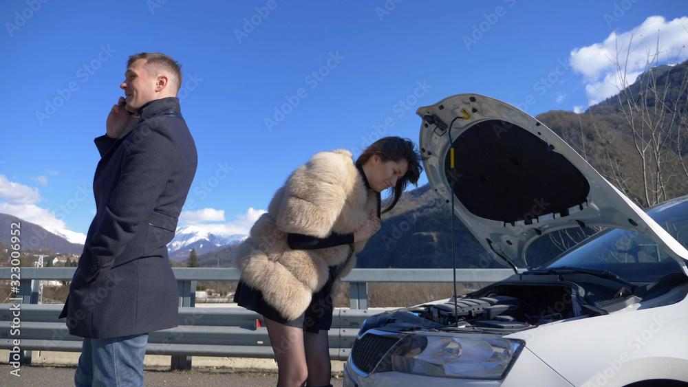 humor. woman looks under the bumper of a car. man talking on the phone