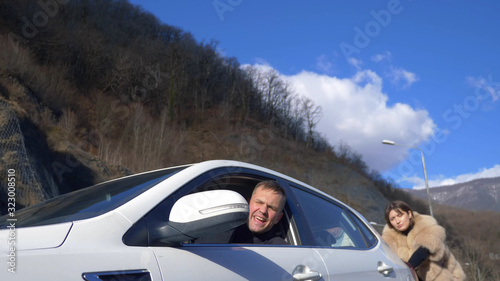 two beautiful girls push the broken car on the road. a man sits behind the wheel