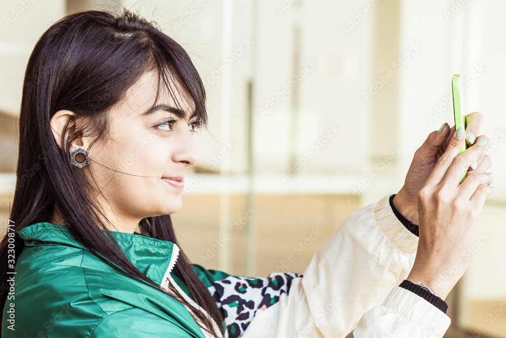 Side view of pretty young mixed-race woman in green jacket making photo on phone. Lifestyle concept Side view of pretty young mixed-race woman in green jacket making photo on phone. Lifestyle concept