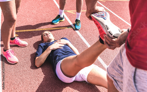 Female athlete injured on athletic run training - Male coach taking care on woman having fatigue cramps  - Sport team concept with young sporty people facing mishaps casualties - Contrast filter photo