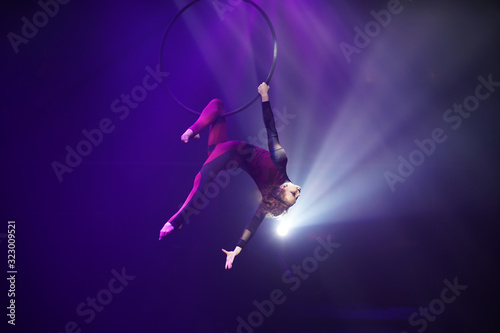 Flexible woman gymnast upside down on hoop, circus show, purple light