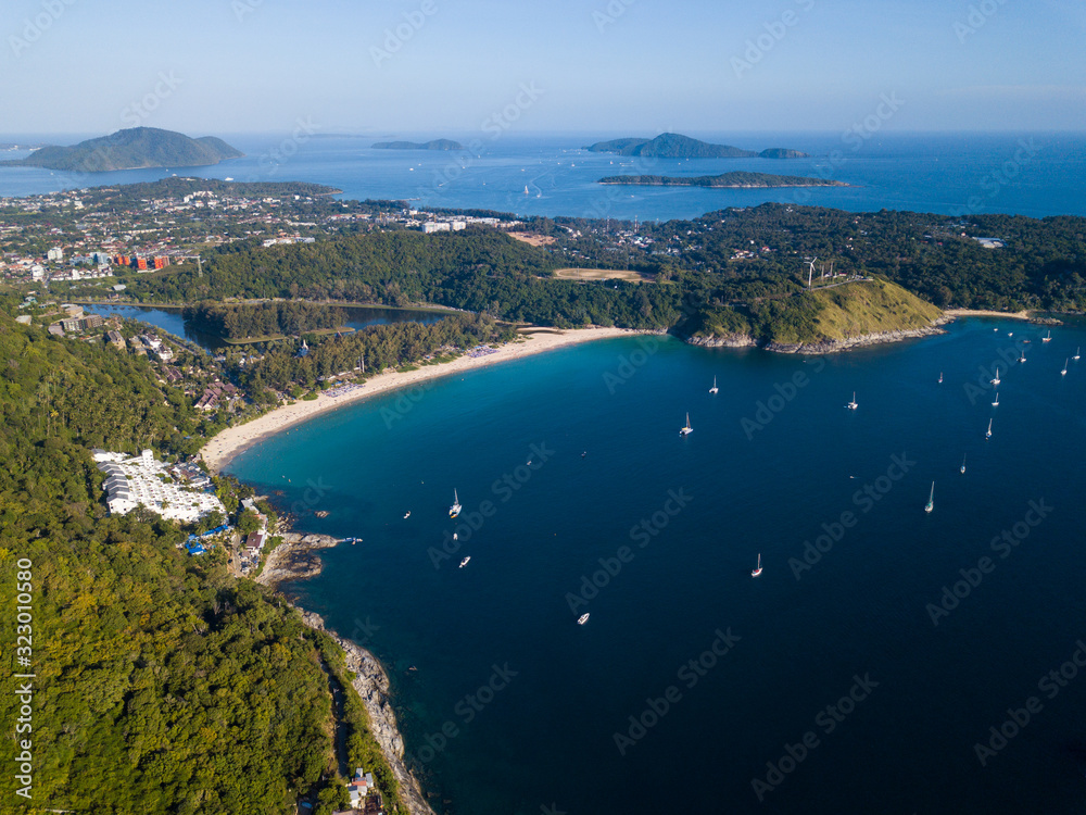 beautiful aerial view of the white sand beach surrounded by green hills, yachts stand in the bay, small islands in the Adaman Sea, Nai Harn Beach, Phuket, Thailand