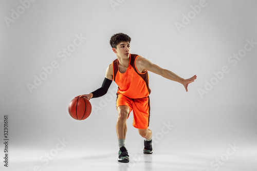 Young basketball player of team wearing sportwear training, practicing in action, motion in run isolated on white background. Concept of sport, movement, energy and dynamic, healthy lifestyle.